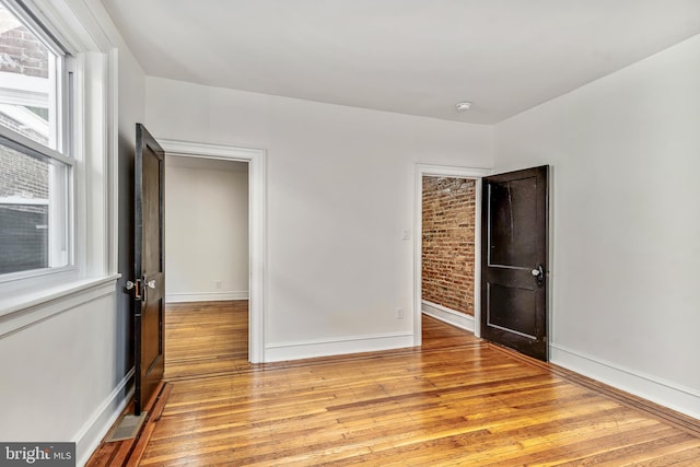 spare room with brick wall and light hardwood / wood-style flooring