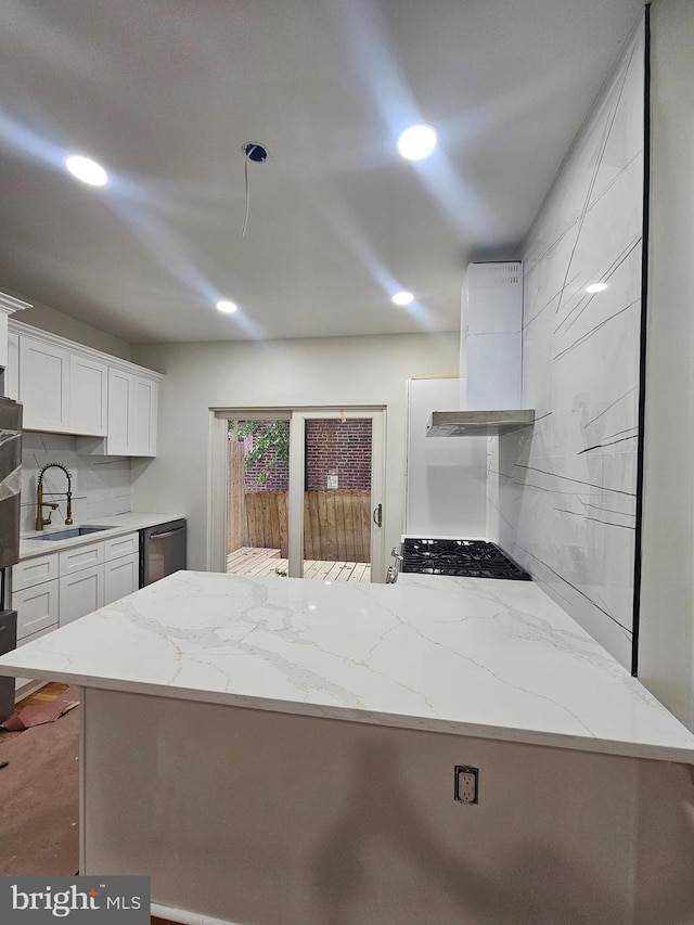 kitchen with kitchen peninsula, range hood, sink, white cabinets, and light stone counters