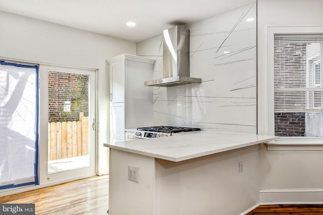 kitchen featuring light stone countertops, wall chimney range hood, stainless steel range oven, kitchen peninsula, and light hardwood / wood-style floors