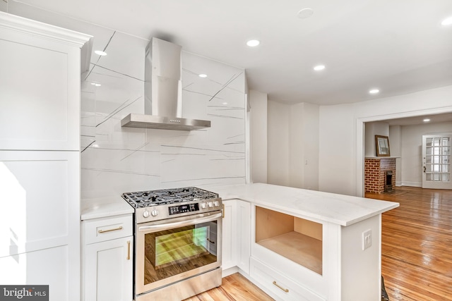 kitchen with white cabinetry, backsplash, stainless steel range with gas stovetop, wall chimney range hood, and light hardwood / wood-style flooring