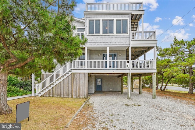 raised beach house featuring a carport, gravel driveway, stairway, and a front lawn