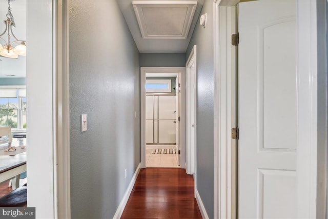 hall featuring a notable chandelier, a textured wall, dark wood-style flooring, and baseboards