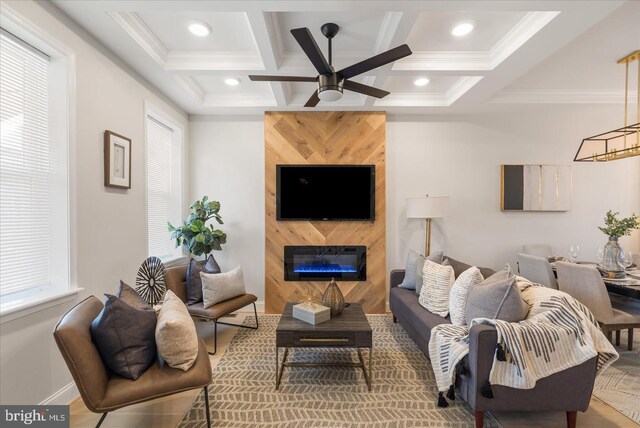 living room featuring a large fireplace, ornamental molding, coffered ceiling, and ceiling fan