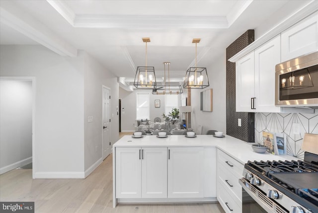 kitchen with light hardwood / wood-style flooring, stainless steel appliances, kitchen peninsula, decorative light fixtures, and a tray ceiling