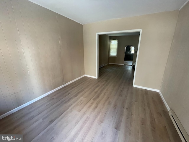 spare room featuring baseboard heating, wood walls, and light hardwood / wood-style floors