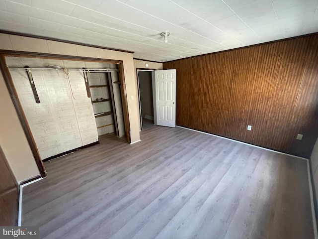 unfurnished bedroom with wood walls, a closet, crown molding, and hardwood / wood-style flooring