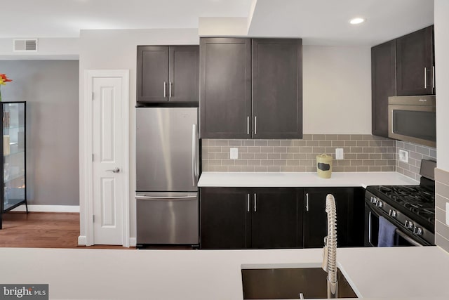 kitchen featuring appliances with stainless steel finishes, hardwood / wood-style floors, sink, backsplash, and dark brown cabinetry