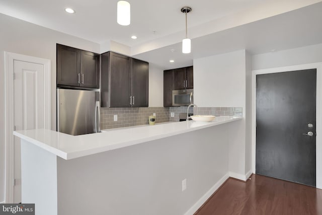 kitchen with tasteful backsplash, stainless steel appliances, pendant lighting, dark hardwood / wood-style floors, and kitchen peninsula