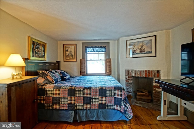 bedroom featuring a brick fireplace, wood-type flooring, and a textured ceiling