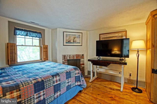 bedroom featuring hardwood / wood-style flooring, a brick fireplace, and a textured ceiling