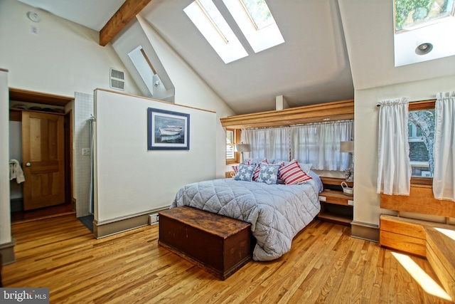 bedroom featuring beamed ceiling, high vaulted ceiling, light hardwood / wood-style floors, and a skylight