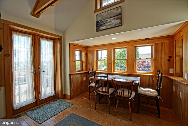 dining room with hardwood / wood-style flooring, lofted ceiling, wooden walls, and french doors