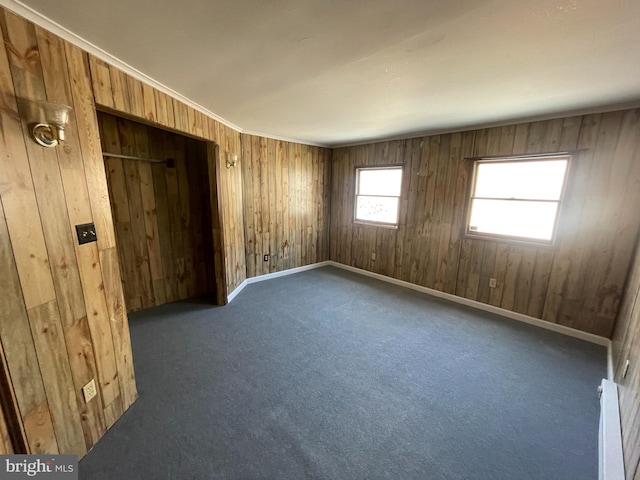 carpeted empty room featuring ornamental molding and wooden walls