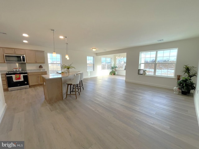 kitchen featuring light hardwood / wood-style floors, a center island with sink, stainless steel appliances, light brown cabinetry, and hanging light fixtures