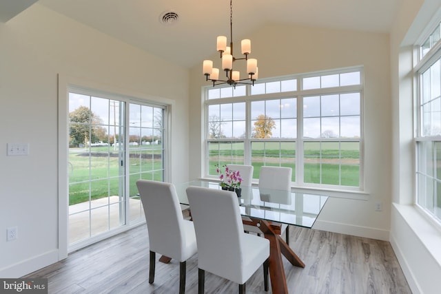 dining room featuring vaulted ceiling, light hardwood / wood-style floors, plenty of natural light, and a notable chandelier