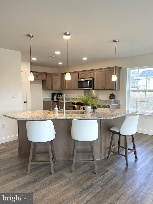 kitchen with decorative light fixtures, dark hardwood / wood-style flooring, and an island with sink