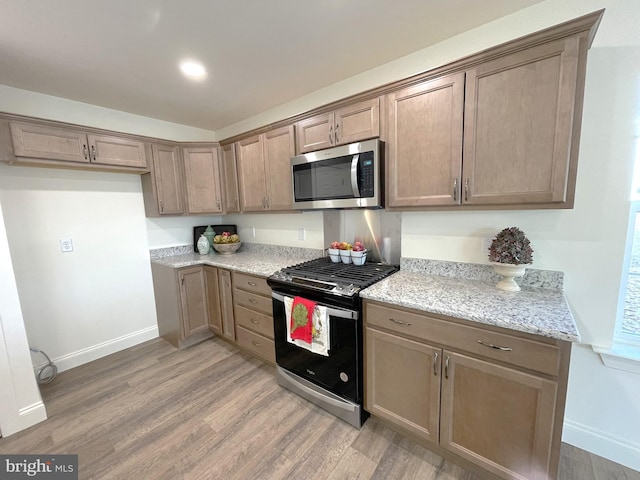 kitchen with light stone counters, stainless steel appliances, and hardwood / wood-style flooring