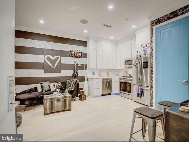 kitchen featuring appliances with stainless steel finishes, white cabinetry, backsplash, light wood-type flooring, and crown molding