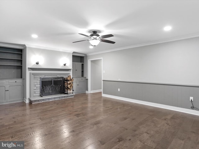 unfurnished living room with a stone fireplace, built in features, ornamental molding, ceiling fan, and dark wood-type flooring