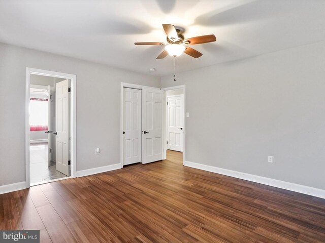 unfurnished bedroom with ceiling fan, ensuite bathroom, and dark hardwood / wood-style flooring