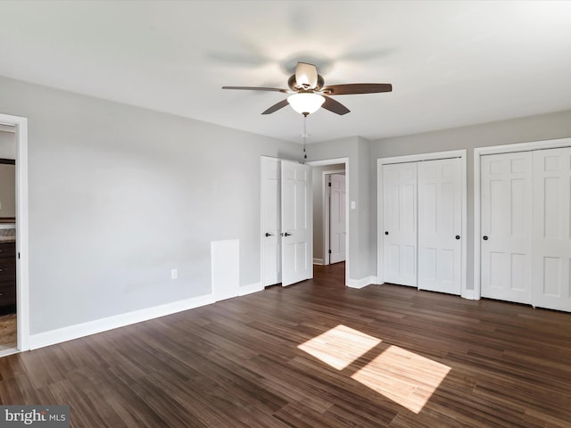 unfurnished bedroom with dark wood-type flooring, two closets, and ceiling fan