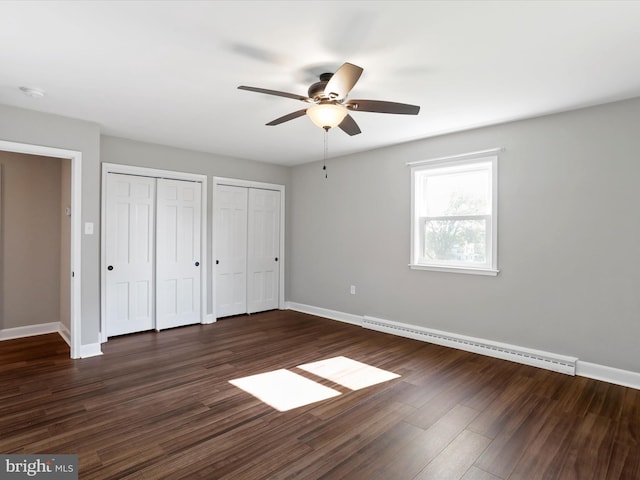 unfurnished bedroom with dark wood-type flooring, ceiling fan, two closets, and a baseboard heating unit