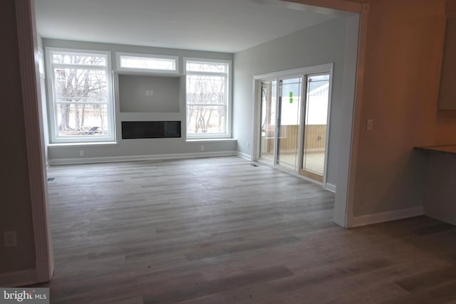 unfurnished living room with a glass covered fireplace, wood finished floors, and baseboards