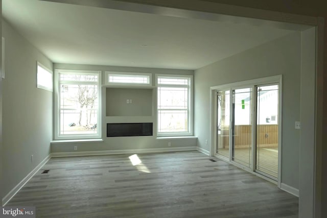 unfurnished living room featuring a healthy amount of sunlight, baseboards, and wood finished floors
