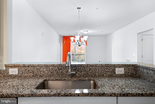 kitchen featuring sink, dark stone counters, an inviting chandelier, and hanging light fixtures