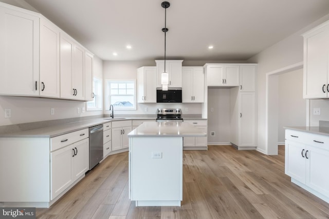 kitchen with stainless steel appliances, sink, pendant lighting, white cabinets, and a center island