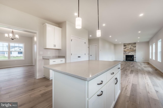 kitchen featuring hanging light fixtures, a kitchen island, white cabinetry, and a stone fireplace