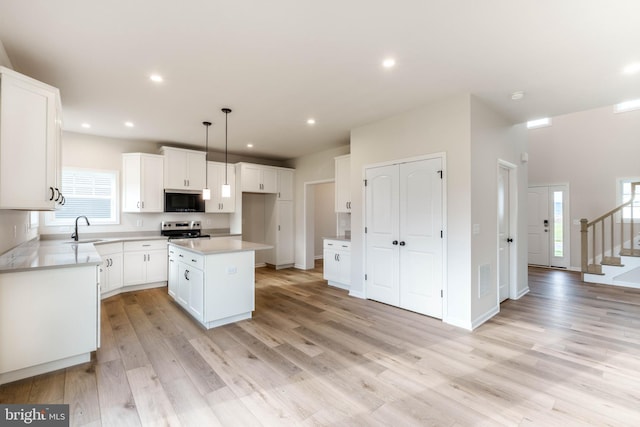 kitchen featuring white cabinets, a kitchen island, stainless steel appliances, sink, and hanging light fixtures