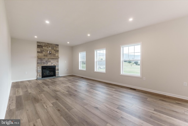 unfurnished living room featuring a stone fireplace and light hardwood / wood-style flooring