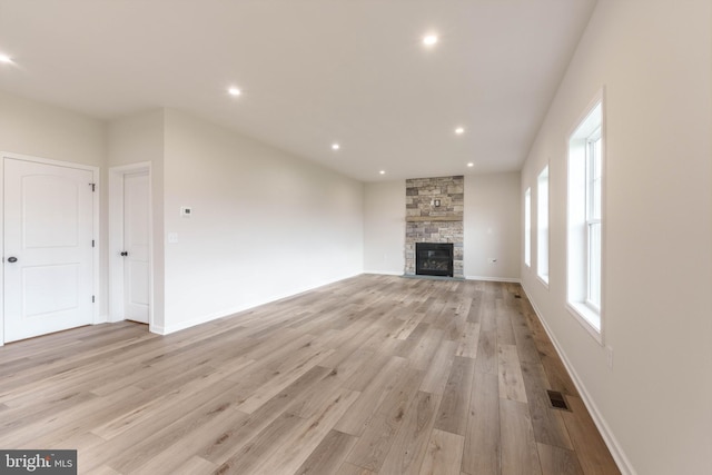 unfurnished living room featuring plenty of natural light, light hardwood / wood-style flooring, and a stone fireplace