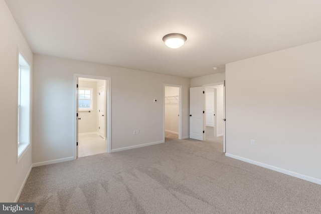 unfurnished bedroom featuring ensuite bathroom, a walk in closet, a closet, and light colored carpet