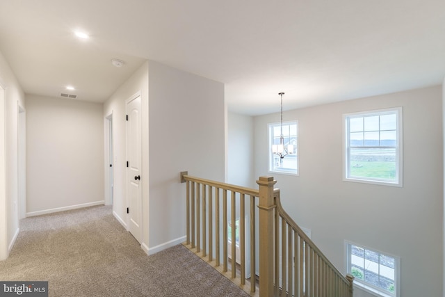 hall with light carpet and a chandelier