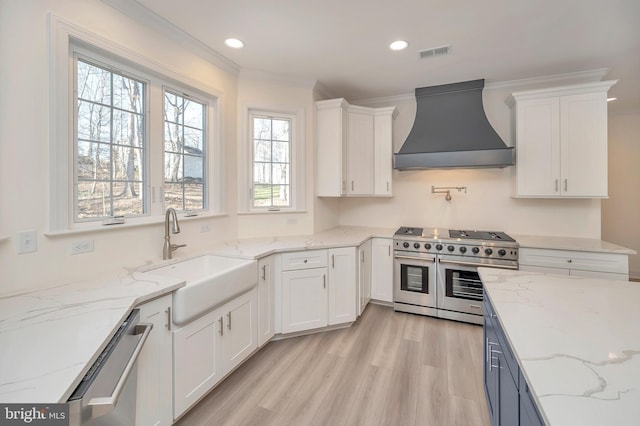 kitchen featuring white cabinetry, stainless steel appliances, wall chimney exhaust hood, light stone counters, and sink