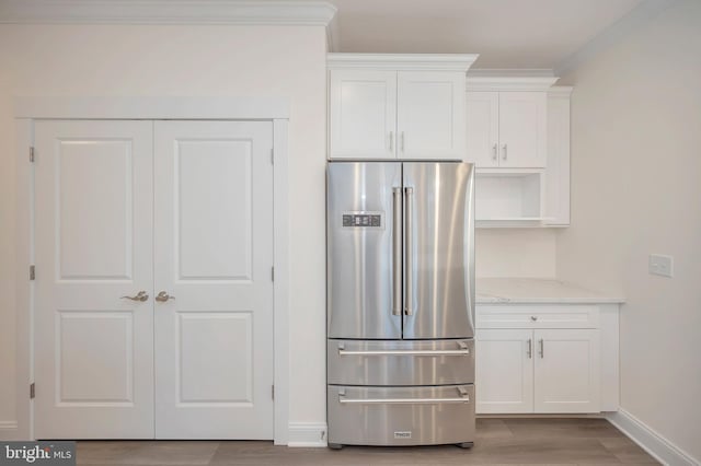 kitchen featuring light stone countertops, white cabinets, ornamental molding, light wood-type flooring, and high end fridge