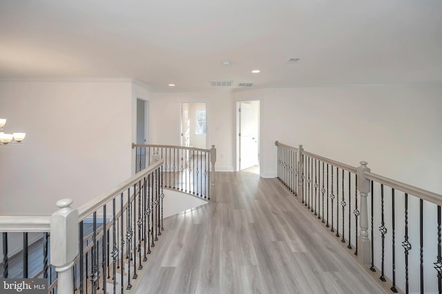 hall with light hardwood / wood-style floors, crown molding, and a chandelier