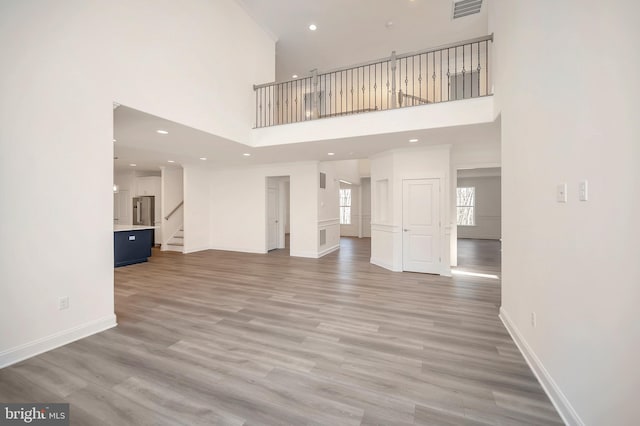 unfurnished living room with light wood-type flooring and a towering ceiling