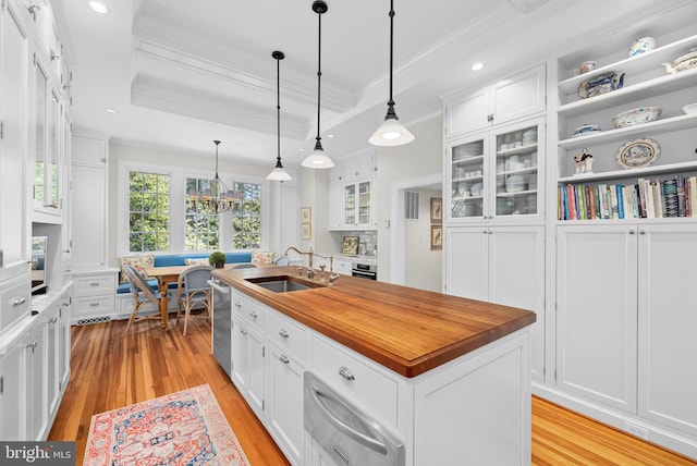 kitchen with sink, white cabinetry, light hardwood / wood-style flooring, hanging light fixtures, and a kitchen island with sink