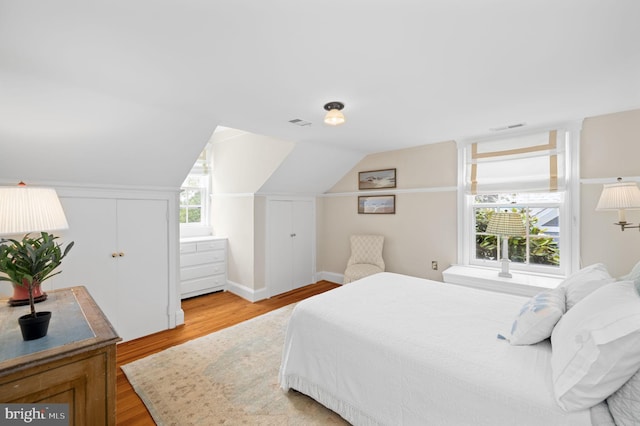 bedroom with lofted ceiling, light hardwood / wood-style floors, and multiple windows