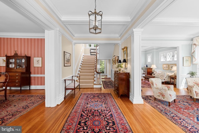 entrance foyer featuring hardwood / wood-style flooring, ornate columns, crown molding, and a notable chandelier