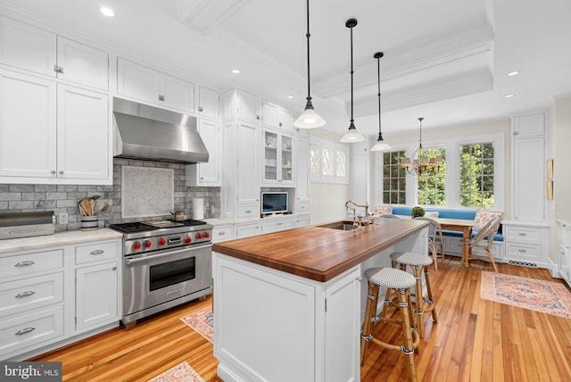 kitchen featuring extractor fan, white cabinetry, an island with sink, premium stove, and butcher block counters