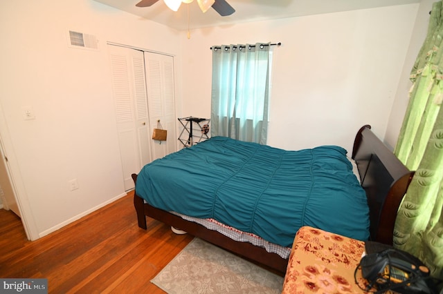 bedroom with a ceiling fan, wood finished floors, visible vents, baseboards, and a closet