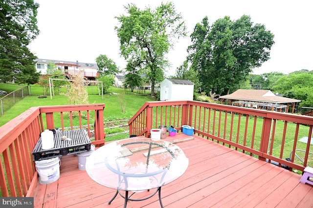 deck with a playground, a lawn, a fenced backyard, an outdoor structure, and a storage unit