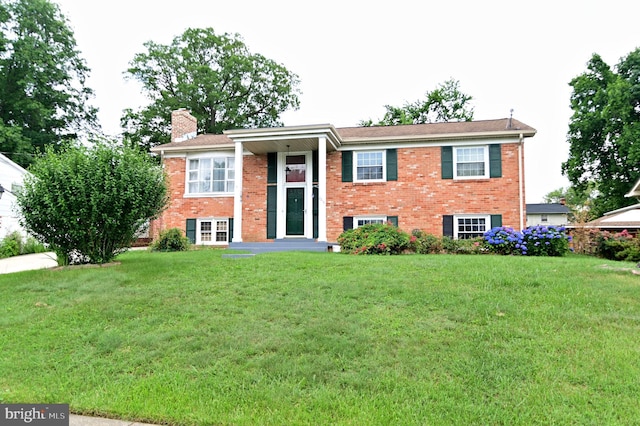 raised ranch featuring brick siding, a chimney, and a front yard