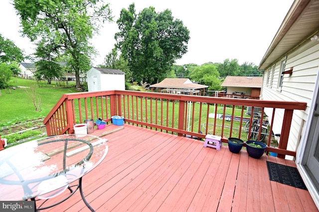 wooden terrace with a storage shed, a yard, and an outbuilding