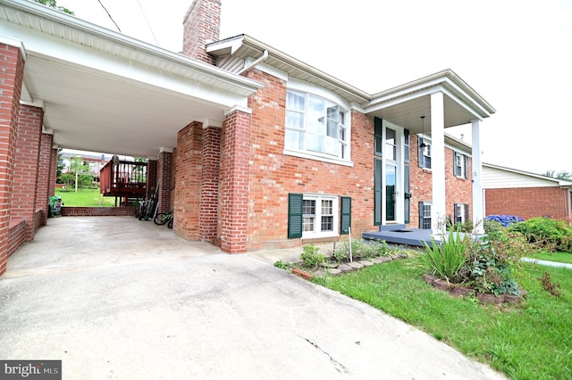 view of front of home featuring concrete driveway, a carport, brick siding, and a chimney