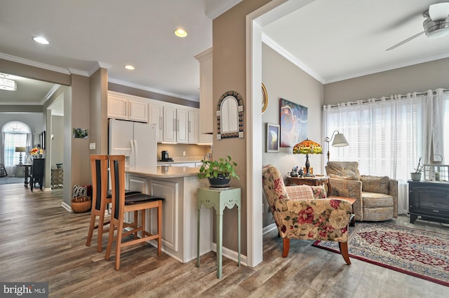 kitchen with a kitchen bar, crown molding, dark hardwood / wood-style flooring, white fridge with ice dispenser, and ceiling fan